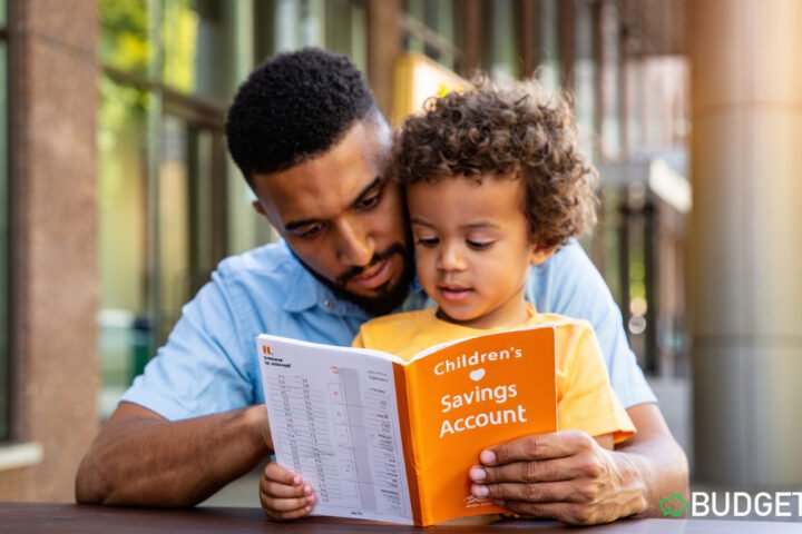 Kids Who Save Early. Parent and child looking at a children’s savings account card at bank