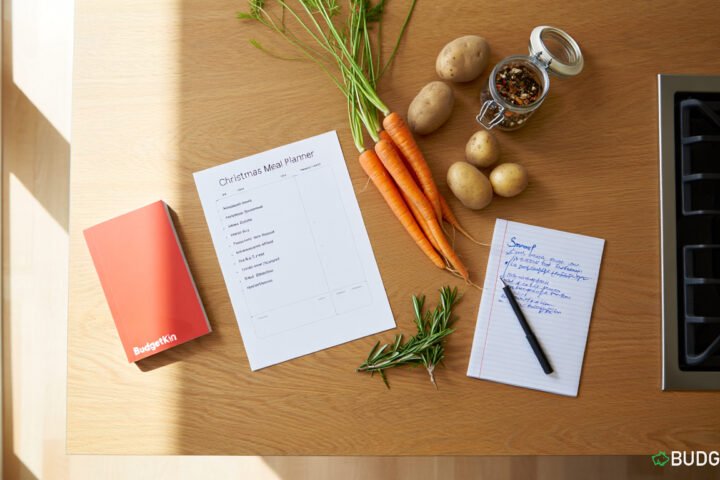 A kitchen counter with a Christmas meal planner, shopping list, fresh vegetables, and recipe notes.