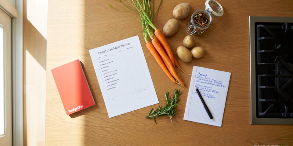 A kitchen counter with a Christmas meal planner, shopping list, fresh vegetables, and recipe notes.