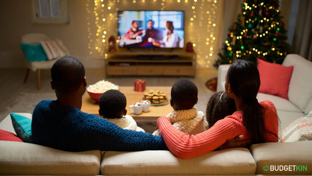 How to Beat Stress at Christmas and Spend Less 6 A family sitting on the sofa under blankets watching a Christmas movie with hot chocolate and warm fairy lights.
