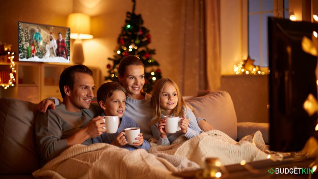 How to Beat Stress at Christmas and Spend Less 2 Family sitting together under blankets watching a Christmas movie, mugs of hot chocolate, simple decorations, small tree, warm lighting, relaxed atmosphere, no excess gifts, low-cost traditions, a peaceful Christmas evening.